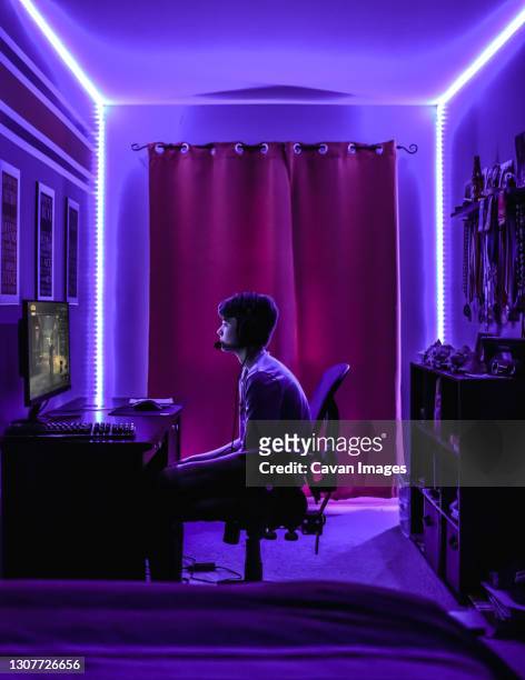 teenage boy playing video game at desk in room with neon led lighting. - gamers stockfoto's en -beelden