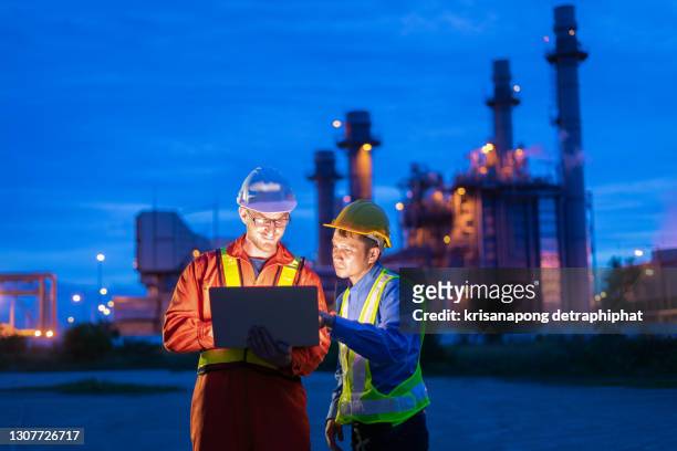 refinery worker,engineer wearing safety helmet using laptop with power plant background, - nuclear power station stock-fotos und bilder