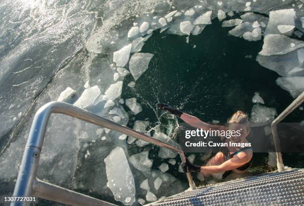 smiling woman making splash with icebergs before swimming in denmark - winter swimming stock pictures, royalty-free photos & images