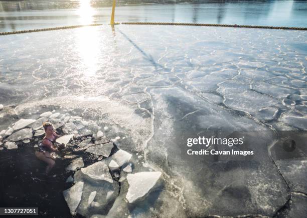 woman holding solid ice while floating in frozen ocean in denmark - winter swimming stock pictures, royalty-free photos & images