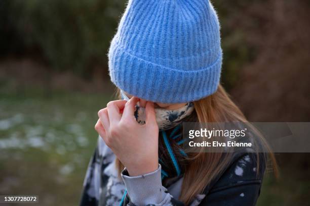 teenage girl wearing protective face mask and rubbing bridge of nose in tension - coronavirus winter stock-fotos und bilder