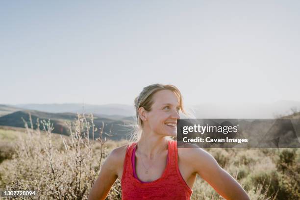 athletic blonde woman laughs with sun and mountains behind her - running in the sun stock-fotos und bilder