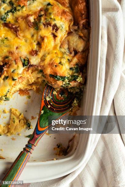 breakfast casserole with eggs sage spinach in a dish with wooden spoon - ovenschotel stockfoto's en -beelden
