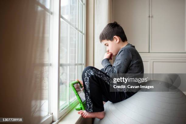 boy 9-10 years old sits on exercise ball playing with his tablet - 12 13 years photos photos et images de collection