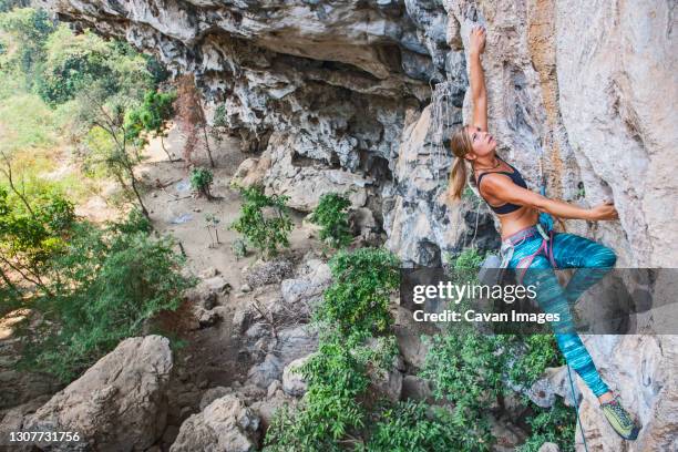 woman climbing steep limestone cliff in laos - overhangende rots stockfoto's en -beelden