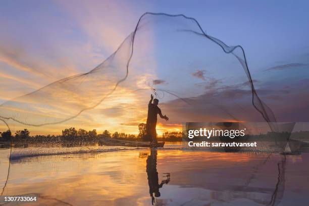 silhouette of a fisherman standing in a boat casting a fishing net at sunset, thailand - fishnet stock pictures, royalty-free photos & images
