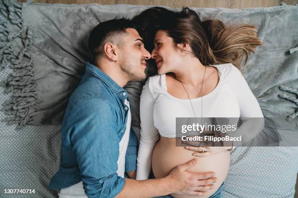 millennial schwangeres paar liegt zusammen auf dem bett - pregnant couple stock-fotos und bilder