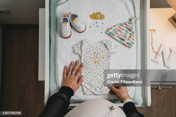 pregnant woman is looking at the clothes of her future baby - baby clothes stock pictures, royalty-free photos & images