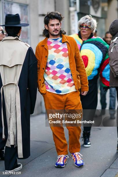 Guest wears a orange large velvet corduroy shirt and pants set, a multicolor check sweater / pullover, Nike orange and navy blue sneakers, outside...