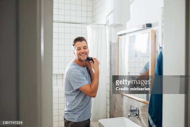 knappe jonge mens die zijn baard met een elektrisch scheermes scheert - shaved stockfoto's en -beelden