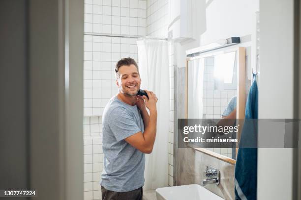 handsome young man shaving his beard with an electric razor - barbuda imagens e fotografias de stock