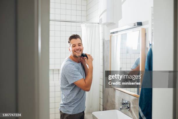 jovem bonito raspando a barba com uma navalha elétrica - clippers - fotografias e filmes do acervo