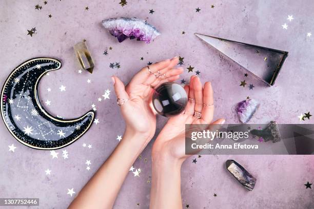 magic crystals for rituals. hands with rings on fingers are holding crystal ball near esoteric set on concrete gray background with many stars sequins. flat lay style - amethyst stock-fotos und bilder