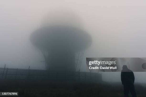 a futuristic concept of a hooded figure standing by a radar base on moorland. on a spooky, foggy day. - weather radar stock pictures, royalty-free photos & images
