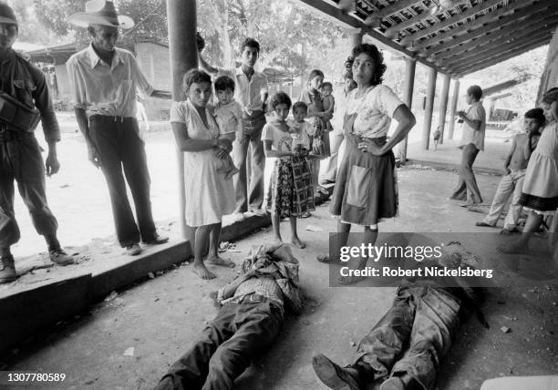 View of a group of people as they stand over of the dead bodies of three civil defensemen, Santa Clara, El Salvador, July 1982. They were killed...