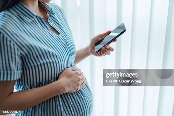 young woman using pregnancy tracker app on smartphone - umstandskleidung stock-fotos und bilder