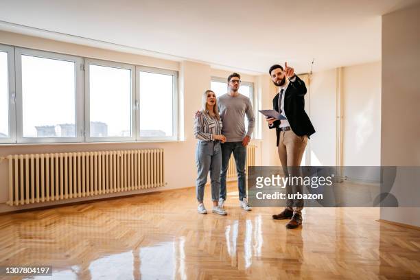real estate agent showing an apartment for sale to a young couple - real estate agent stock pictures, royalty-free photos & images