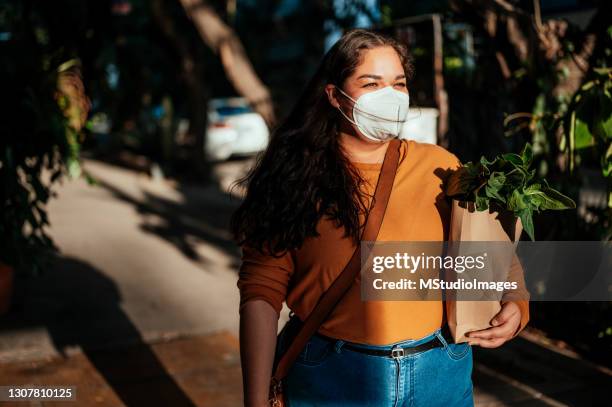 woman wearing protective face mask and holding groceries - n95 face mask stock pictures, royalty-free photos & images