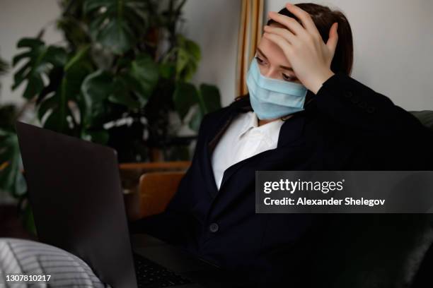 portrait of nice lady indoors with medical protective facial face mask. woman is working on portative laptop computer. new normal concept. girl is stressed in depression - bullying workplace stock pictures, royalty-free photos & images