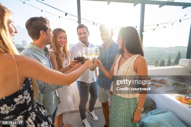 a group of friends toasting with red and white wine outdoors on a rooftop. - happy hour stock pictures, royalty-free photos & images