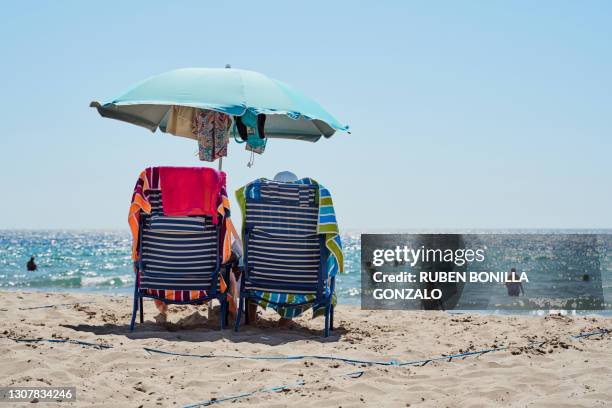 parasol, two chairs and towels on sand beach while tourists having bath in sea in summer - benidorm photos et images de collection