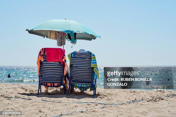 parasol, two chairs and towels on sand beach while tourists having bath in sea in summer - beach seat stock pictures, royalty-free photos & images