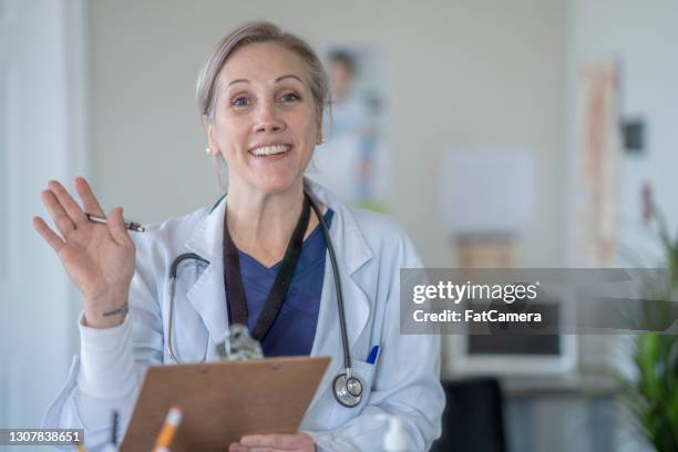 friendly female caucasian doctor waving to welcome patients - waving hi stock pictures, royalty-free photos & images