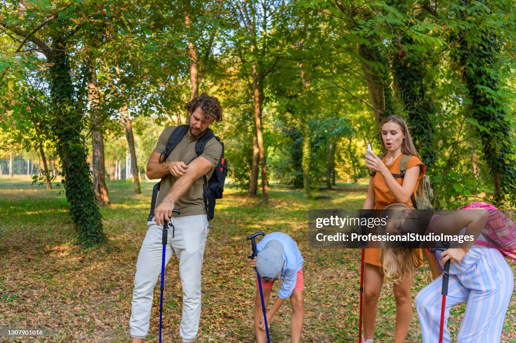 A Young Father and Mother with Children are Traveling with Backpacks and have Problems with Insects in the Forest.