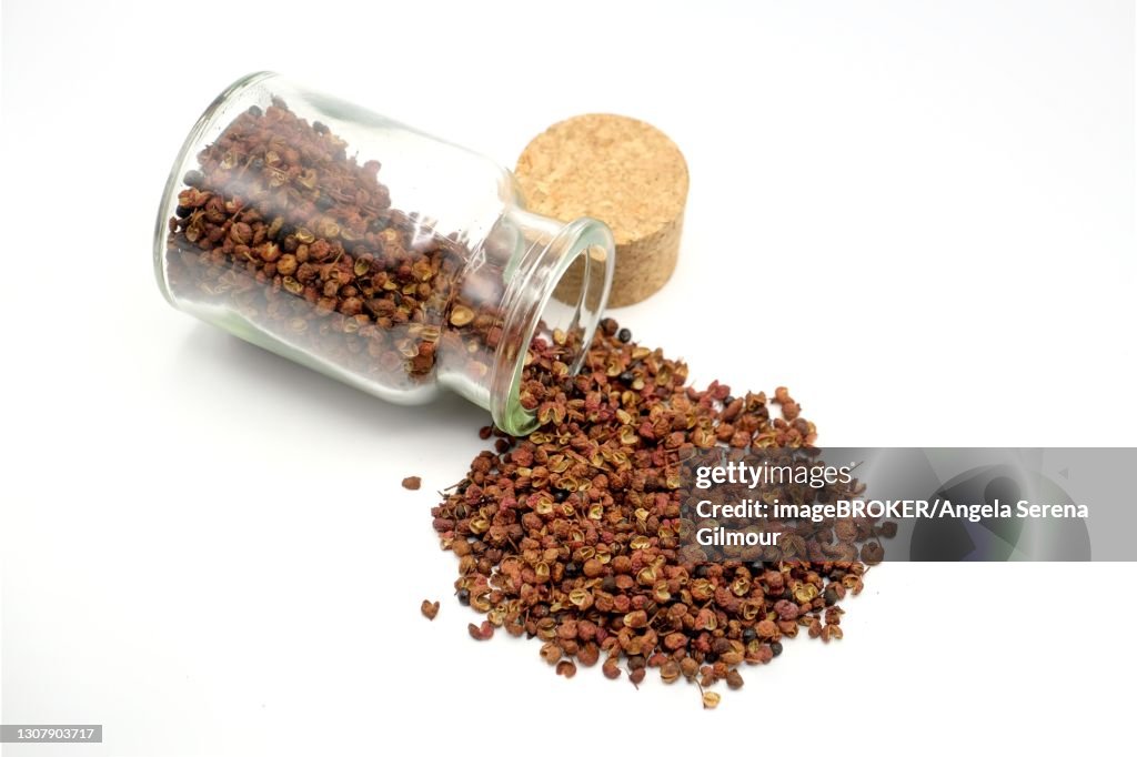 Sichuan peppercorns spilling out of a 150ml glass spice jar against a white background, Germany