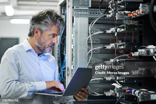 engineer with laptop examining in server room - server stock-fotos und bilder