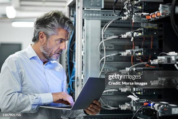 engineer with laptop examining in server room - computer cable foto e immagini stock