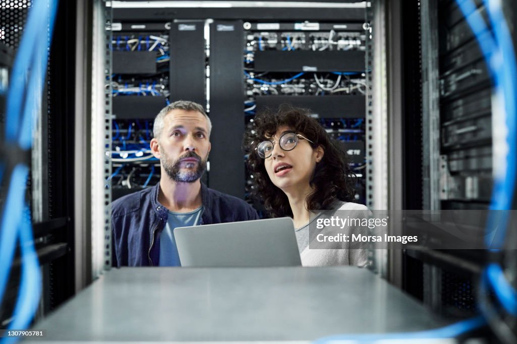 Female technician discussing with male coworker in server room