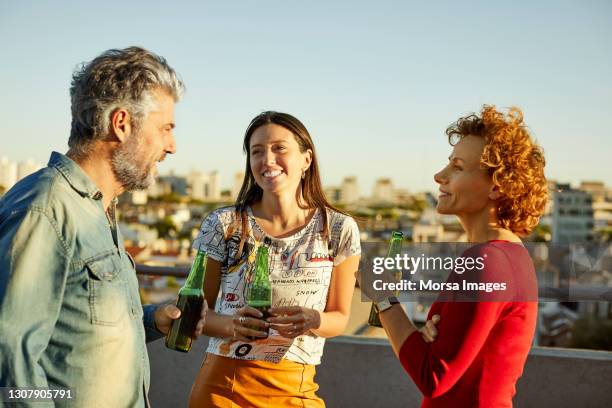 friends with beer talking on rooftop - man sipping beer smiling stockfoto's en -beelden