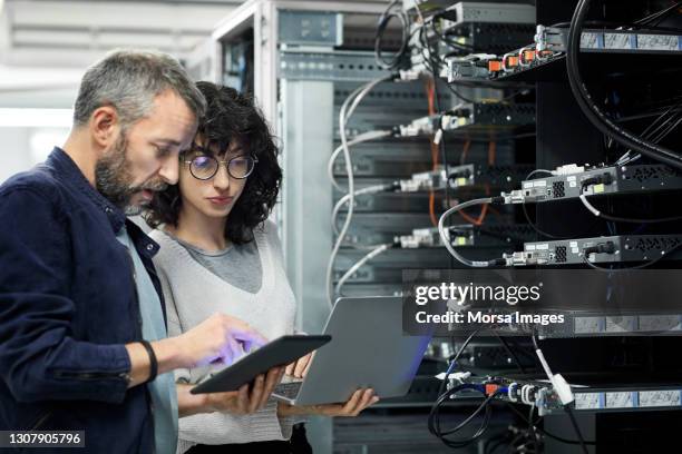 male technician showing digital tablet to coworker in server room - technician stock pictures, royalty-free photos & images