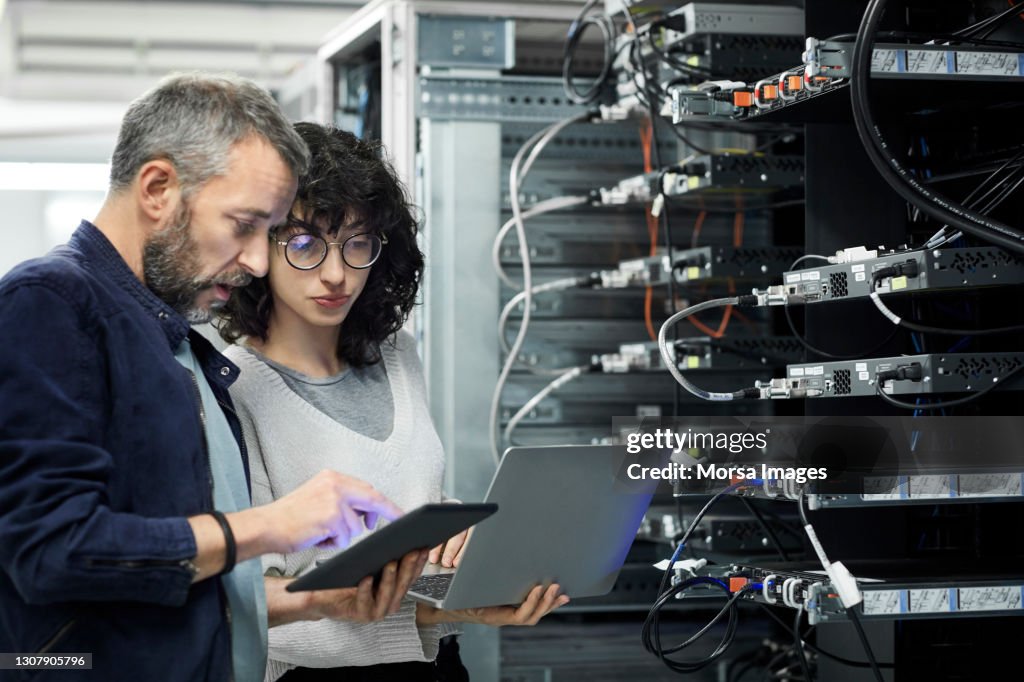 Male technician showing digital tablet to coworker in server room