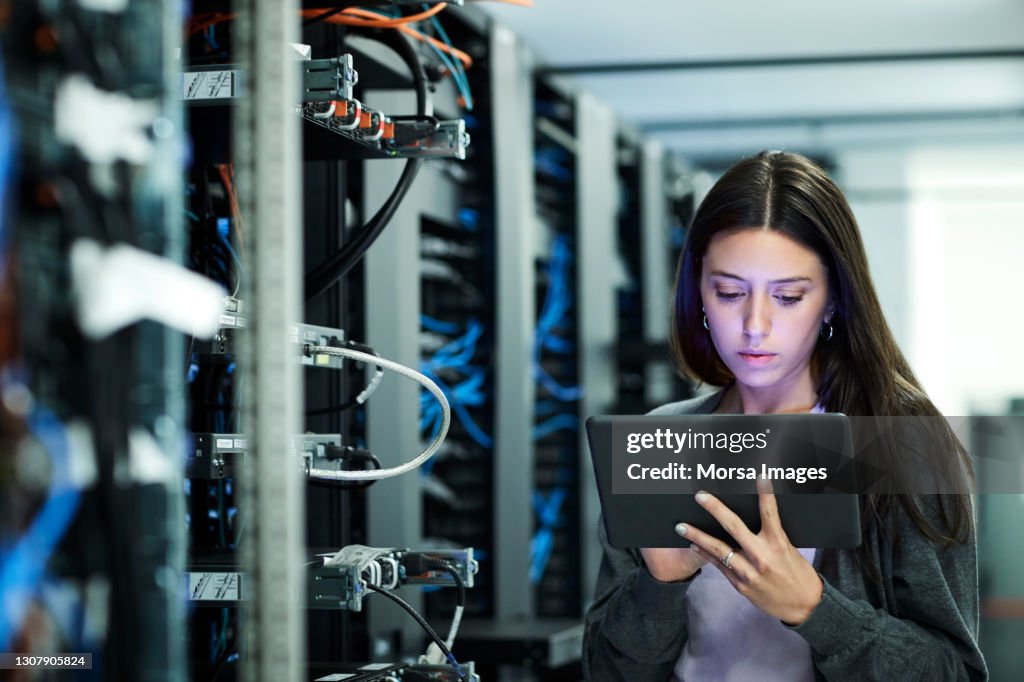 Female technician using digital tablet examining in server room