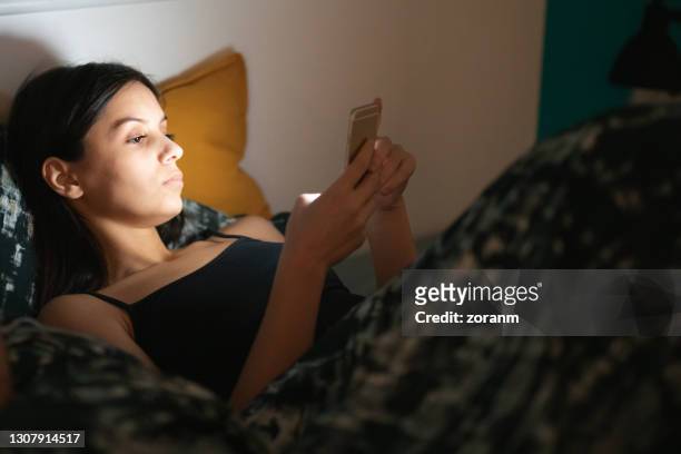 年輕女子晚上躺在床上，使用在線約會應用程式 - scrolling 個照片及圖片檔