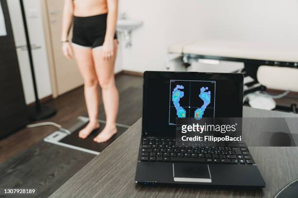 la giovane donna adulta è in piedi su uno scanner a pressione medica per analizzare la sua impronta e realizzare nuove solette per scarpe per migliorare la sua postura - piedi foto e immagini stock