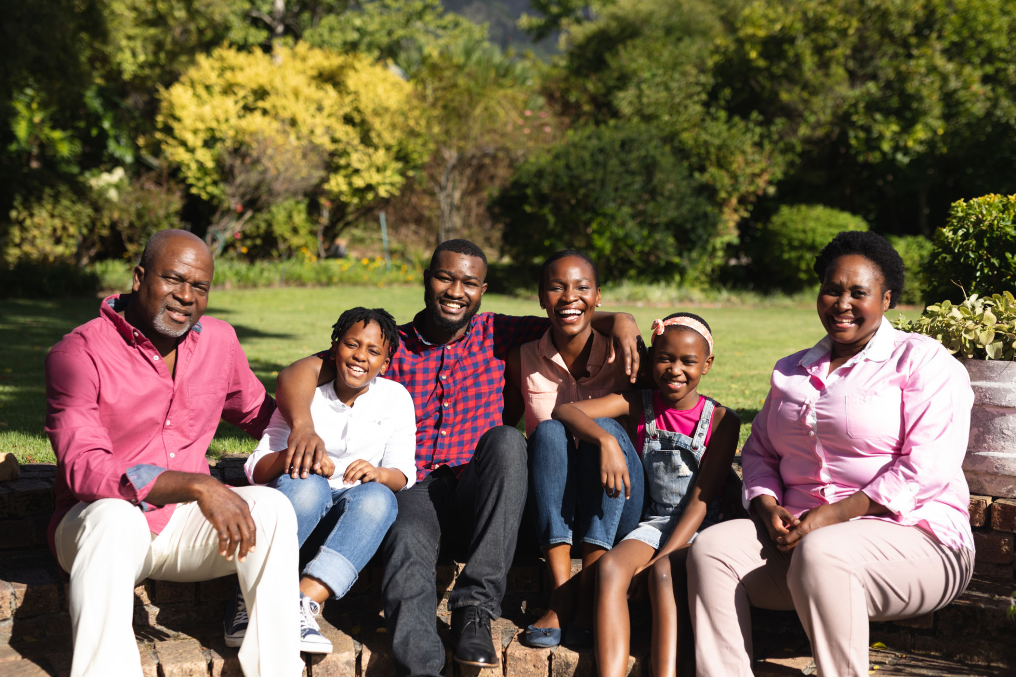 Smiling african american parents with children and their grandparents sitting embracing outdoors Smiling african american parents with children and their grandparents sitting embracing outdoors