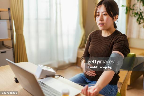 jeune femme enceinte parlant avec le docteur sur l’ordinateur portatif et vérifiant sa tension artérielle - blood pressure photos et images de collection