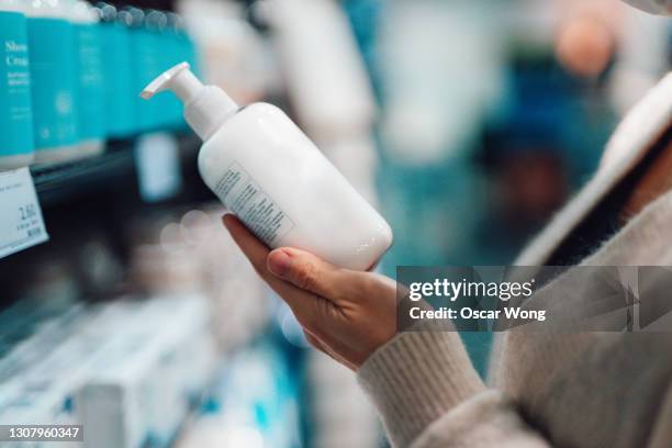 close-up shot of female hand holding hand cream bottle in supermarket - magasin cosmétique photos et images de collection