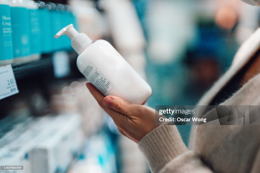 Close-up Shot Of Female Hand Holding Hand Cream Bottle In Supermarket