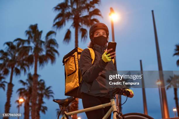 a delivery biker with a covid protection mask at night. - bicycle messenger stock pictures, royalty-free photos & images