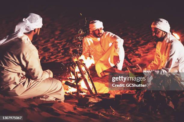 arab friends seated around campfire at a desert camp - abu dhabi night stock pictures, royalty-free photos & images