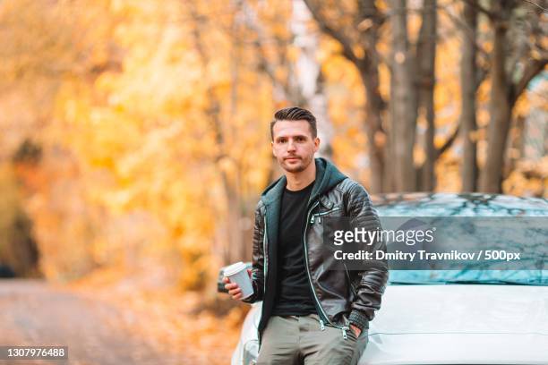 young man drinking coffee with phone in autumn park outdoors - coffee car design stock pictures, royalty-free photos & images