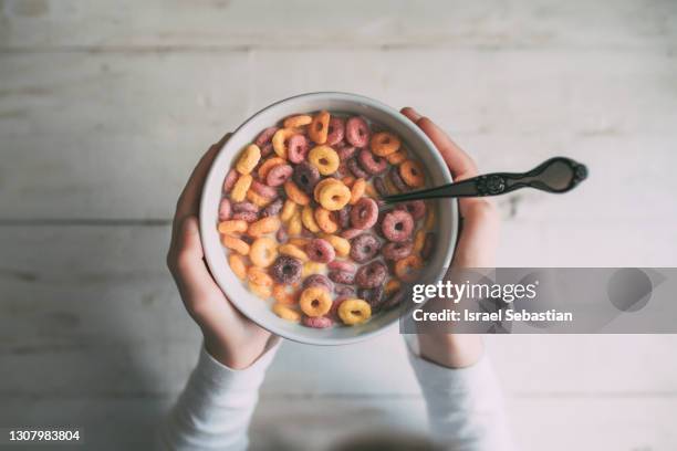 view from above of an unrecognizable little girl eating colorful ring-shaped cereal in a bowl of milk for breakfast. domestic life - breakfast cereal stock pictures, royalty-free photos & images