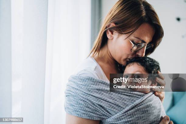 madre besando a su hijo en cabestrillo. - portabebés fotografías e imágenes de stock