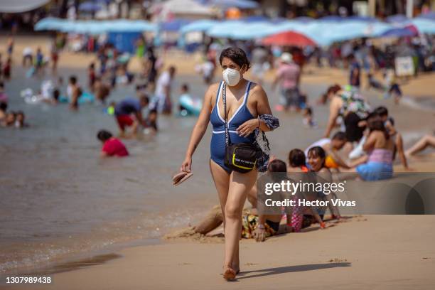 Tourist in a bathing suit wearing a mask walks along Caleta beach on March 19, 2021 in Acapulco, Mexico. Acapulco began its vaccination plan for...