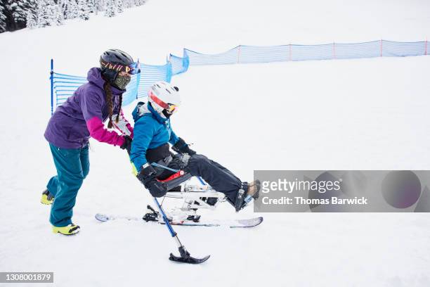 full length view of friend helping female adaptive athlete move uphill on monoski before going skiing - womens us ski team stock pictures, royalty-free photos & images