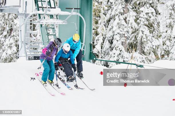 full length view of friends helping female adaptive athlete on monoski off of chairlift while skiing at resort on winter morning - womens us ski team stock pictures, royalty-free photos & images